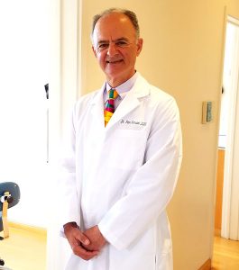 Dr. Peter A. Karsant wearing a lab coat and a colorful tie, smiling